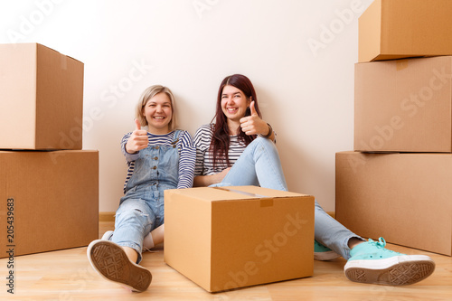 Photo of young blonde and brunette on floor among cardboard boxes