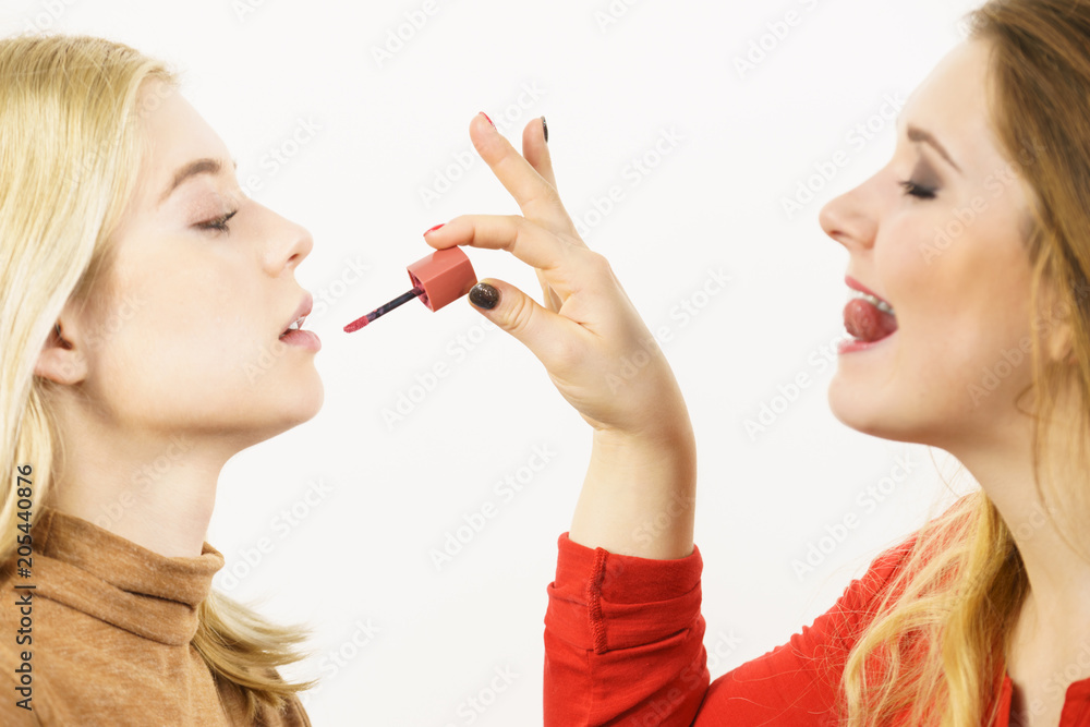 Woman applying her friend lipstick on lips Woman applying her friend lipstick on lips