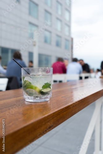 Картината върху платно Mojito Cuban cocktail with fresh mint and black cocktail straw in a tumbler sitting on a wooden table outside on a trendy rooftop bar in New York
