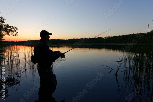 Silhouette of fisherman standing in the lake and catching the fish during sunset © mtmmarek