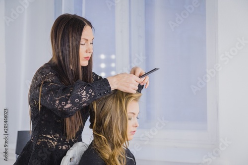 Professional hairdresser, stylist combing hair of female client in white make up room. Beauty and haircare concept