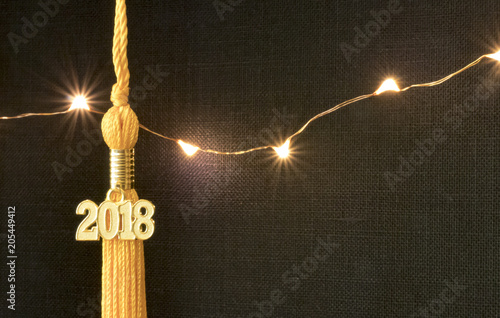 Class of 2018. Gold tassel drop graduation gown accessory and keepsake against a black textured background and lights. Iconic symbol of a graduate's academic and life success. photo