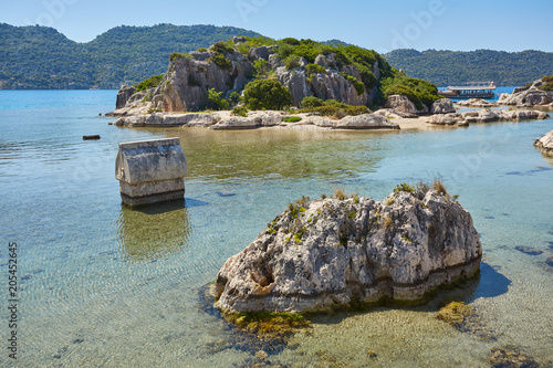 Lycian stone sarcophagus with pointed lid of the roman era popping up from the green water in the harbor of Kalek y-Castle Village or ancient Simena city. photo