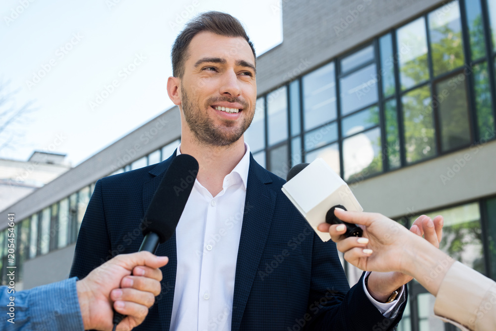 Fototapeta premium two journalists interviewing successful businessman with microphones