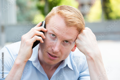 Closeup portrait, young man annoyed, frustrated, pissed off by someone talking on his mobile phone, bad news, isolated outdoors outside background. Long wait times, horrible conversations concept © ashtproductions