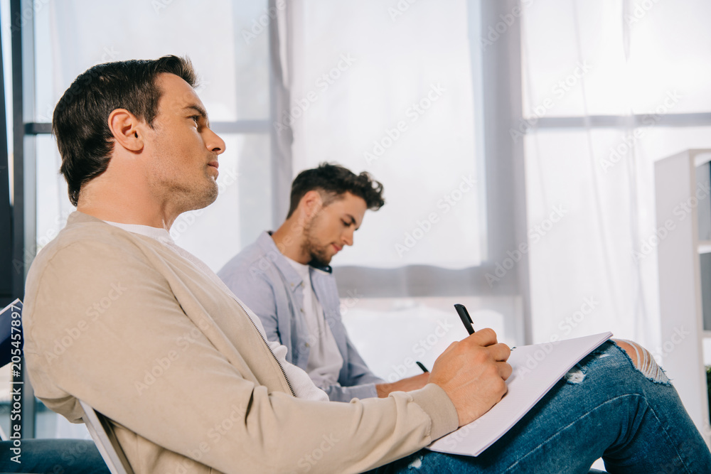 side view of businessmen with notebooks at business training in office side view of businessmen with notebooks at business training in office