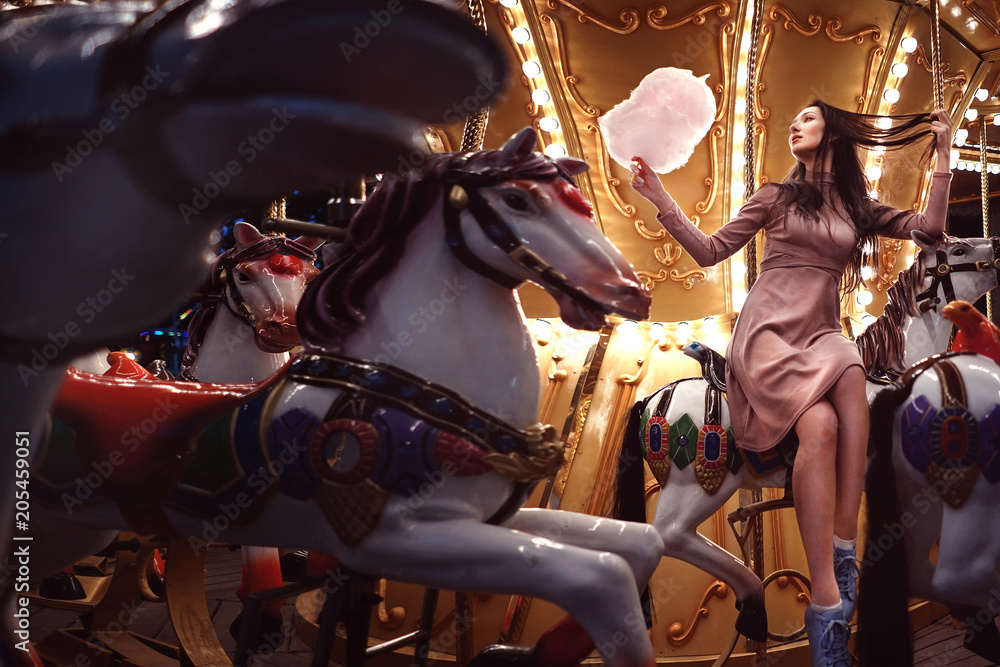 Young beauty model woman posing with old horse carousel in summer park with magic lights Young beauty model woman posing with old horse carousel in summer park with magic lights