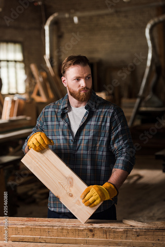 carpenter in protective gloves working with wooden plank at sawmill