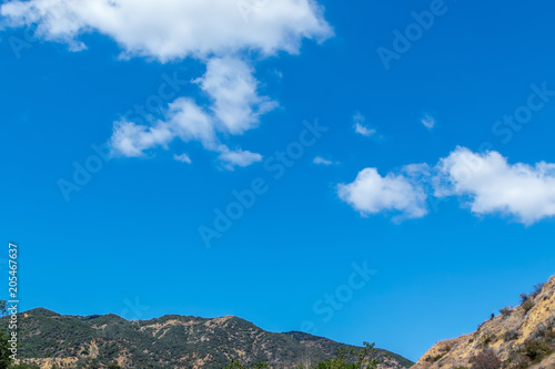 Big blue sky and white clouds with mountains on bottom border and room for text