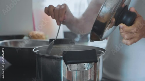 Hand with spoon stirring boiling soup, close-up.