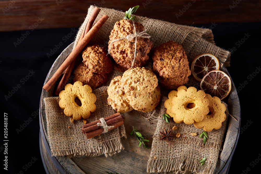 Conceptual composition with assortment of cookies and cinnamon with napkin on a wooden barrel, selective focus Conceptual composition with assortment of cookies and cinnamon with napkin on a wooden barrel, selective focus