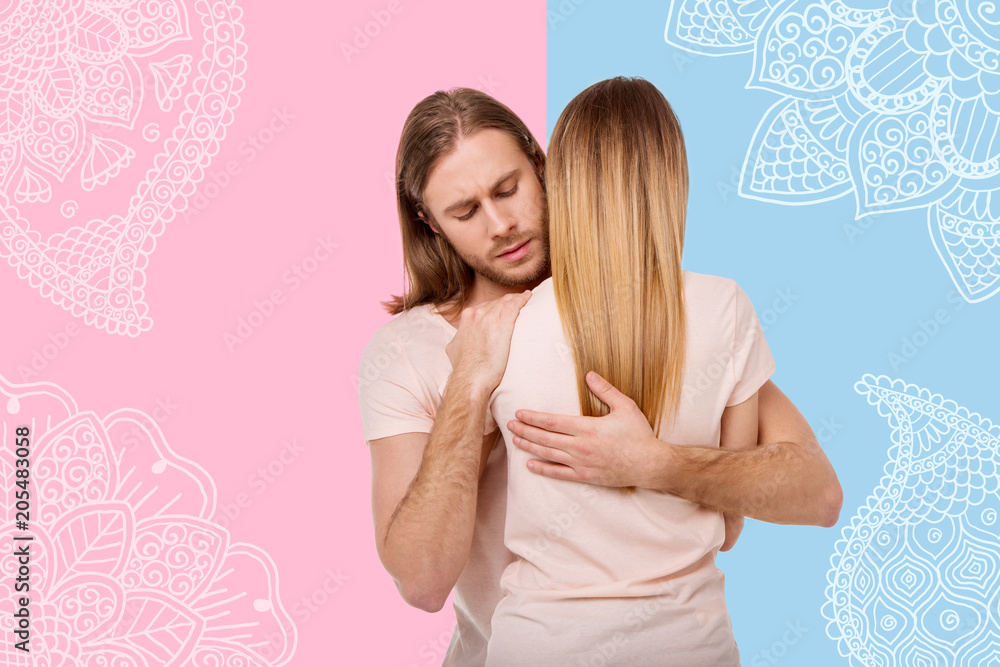Warm hugs. Young serious man frowning and staying calm while hugging and comforting his jobless wife Warm hugs. Young serious man frowning and staying calm while hugging and comforting his jobless wife