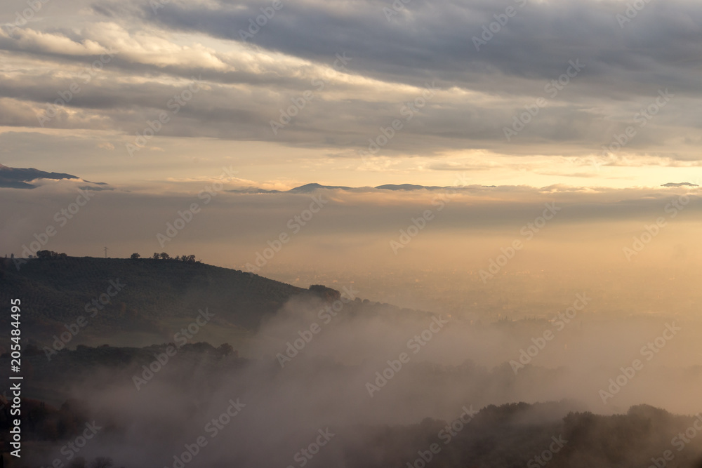 A valley in autumn filled by mist at sunset, with emerging hills