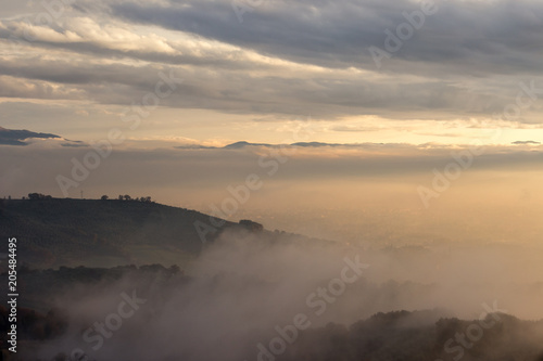 A valley in autumn filled by mist at sunset, with emerging hills