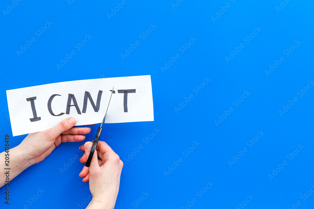 I can concept. Motivate youself, believe in yourself. Hand cut off the letter t of written word I can't by sciccors. Blue background top view copy space I can concept. Motivate youself, believe in yourself. Hand cut off the letter t of written word I can't by sciccors. Blue background top view copy space
