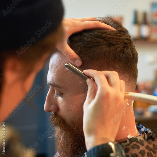 Close up of a hairdresses work for an attractive young blond man at the barber shop. He is doing styling of his beard, shaving with straight razor