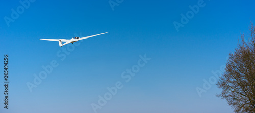 Pure white Glider in clear blue sky flying over the treetop. Concept of success, achievement of high goal