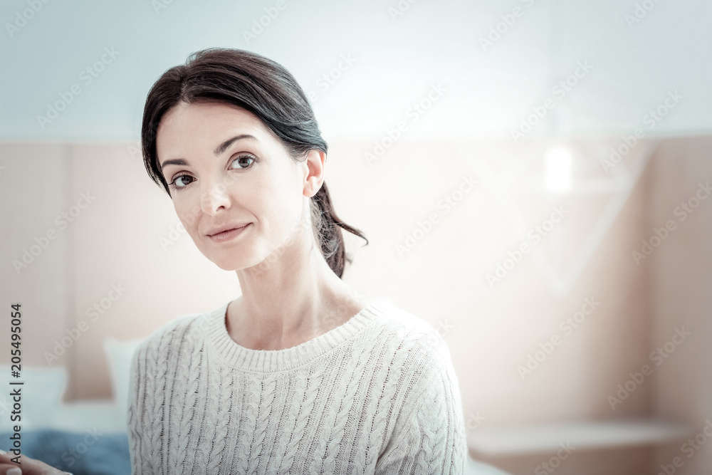 Pleasant smile. Charming female person sitting on the bed and bowing head while expressing positivity Pleasant smile. Charming female person sitting on the bed and bowing head while expressing positivity