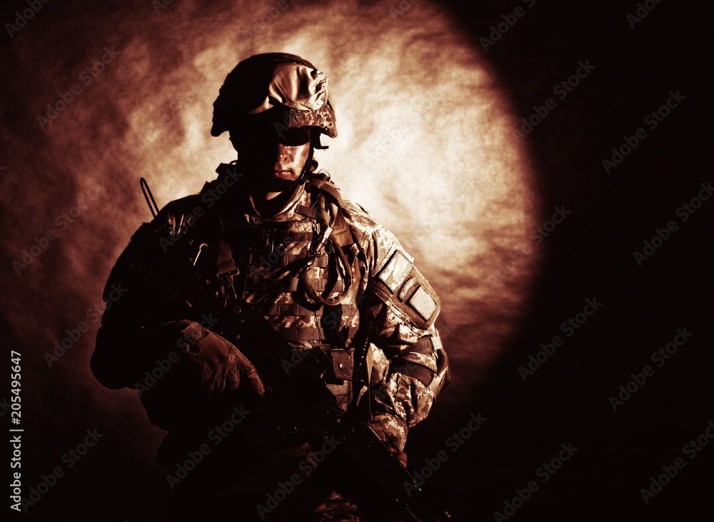Low key studio portrait of private security service contractor, army infantry rifleman, US marine raider in helmet, sunglasses, camouflage uniform posing with weapon on black background with backlight Low key studio portrait of private security service contractor, army infantry rifleman, US marine raider in helmet, sunglasses, camouflage uniform posing with weapon on black background with backlight