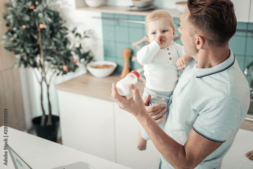 Hey you. Competent young father standing in semi position and holding his baby while being at home Hey you. Competent young father standing in semi position and holding his baby while being at home