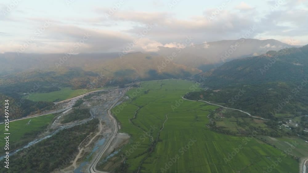 Aerial view of farmer fields, river, village in the background of mountains at sunset on the island of Luzon, Philippines. Mountain landscape with valley and village. Aerial view of farmer fields, river, village in the background of mountains at sunset on the island of Luzon, Philippines. Mountain landscape with valley and village.