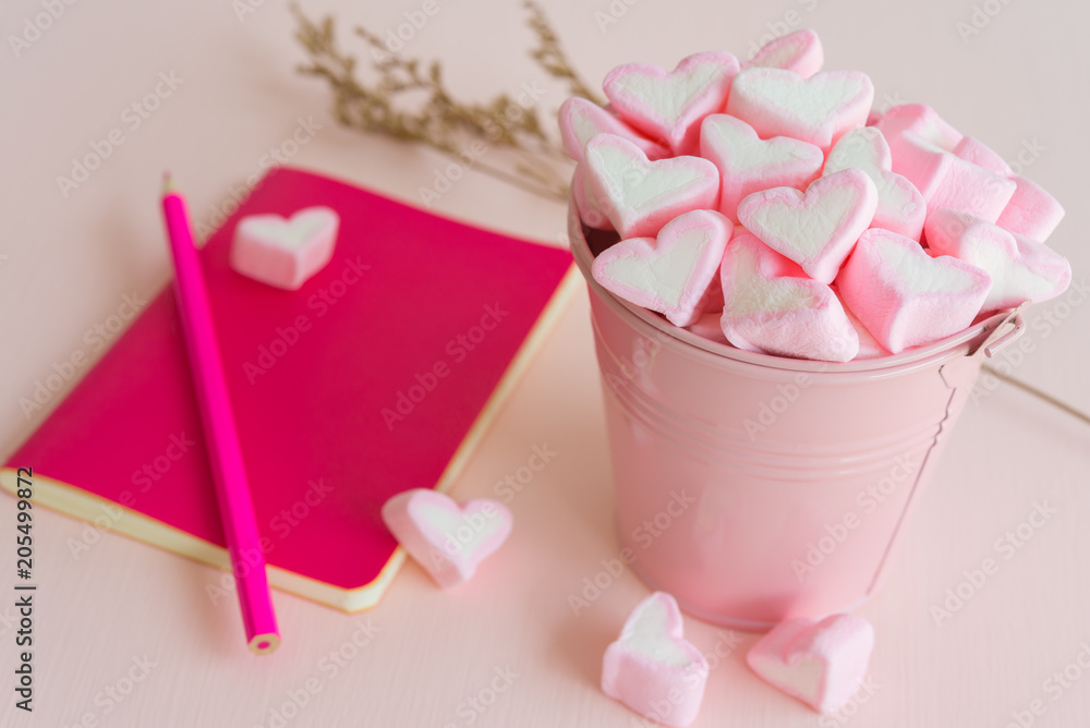 Fluffy pink heart marshmallow in small tank and pink notepad, pencil on pink background Fluffy pink heart marshmallow in small tank and pink notepad, pencil on pink background