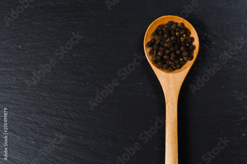 Black pepper spice in wooden spoon on dark stone table