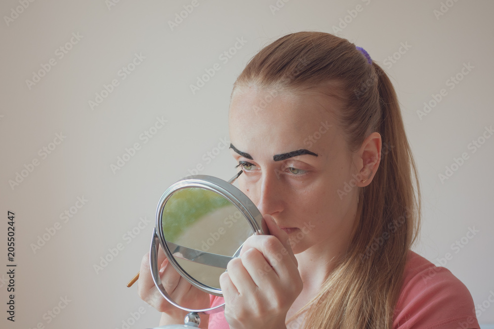 Woman is painting her eyebrows and looking in the mirror, close-up photo Woman is painting her eyebrows and looking in the mirror, close-up photo