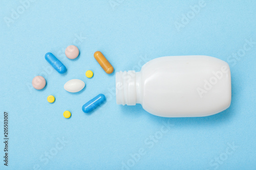 White bottle with different pills and capsules on blue background