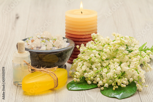 Soap, bottle with aromatic oil, bowl with sea salt, burning candle and bouquet of lilies of the valley