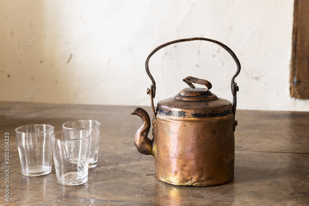 Still life with a beautiful worn retro style copper tea kettle with three empty glasses on a massive wooden table. Still life with a beautiful worn retro style copper tea kettle with three empty glasses on a massive wooden table.
