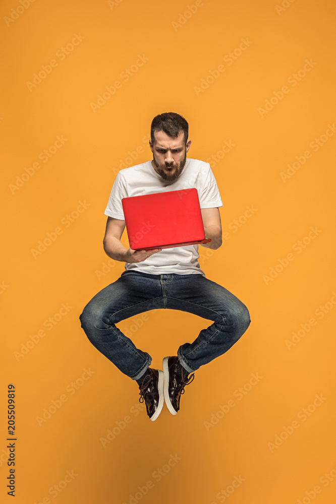 Image of young man over orange background using laptop computer while jumping. Image of young man over orange background using laptop computer while jumping.