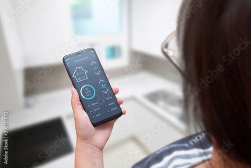 Woman use smart home control app on modern mobile phone. Home interior in background.