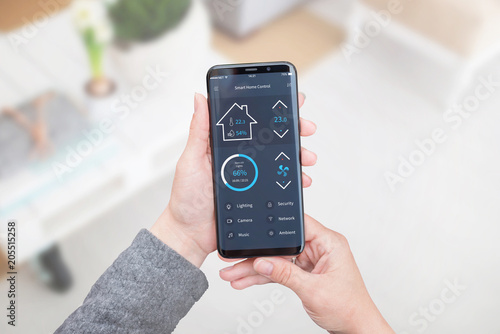 Smart home control app for mobile devices in woman hand. Living room interior in background.