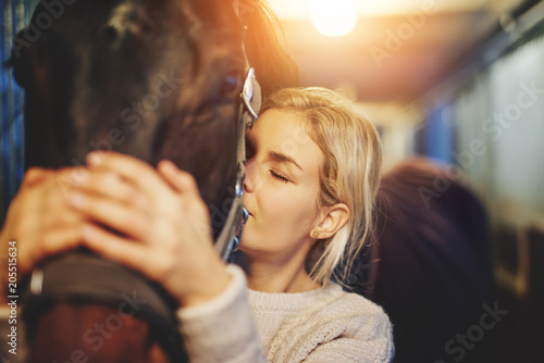 Young woman hugging her horse in stables before a ride