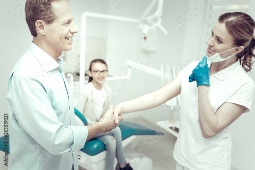 Thank you. Happy smiling grateful patient shaking hands with his experienced professional dentist in a modern dental clinic
