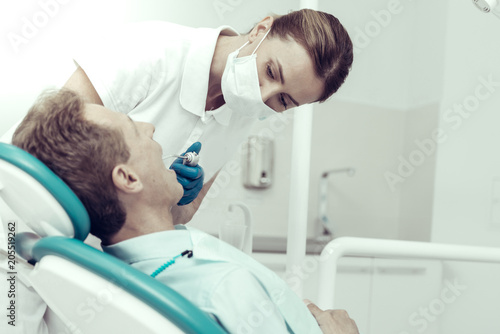Complete attention. Careful concentrated dentist looking into the mouth of her patient while curing him with a help of a dental engine