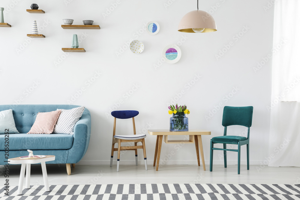 Sofa next to a sitting corner with chairs and table decorated with flowers in a pastel living room interior with shelves and wall decorations Sofa next to a sitting corner with chairs and table decorated with flowers in a pastel living room interior with shelves and wall decorations