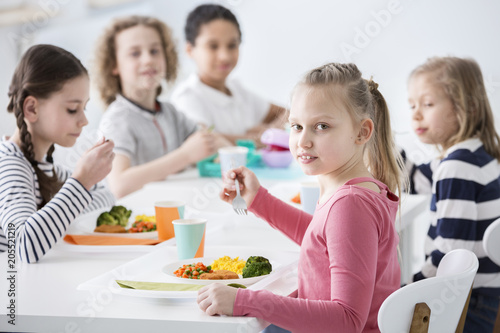 Girl eating vegetables with friends in the canteen during break at school