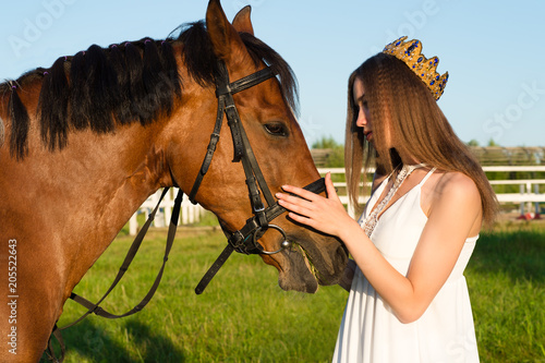 beautiful girl with a crown caress horse outdoors