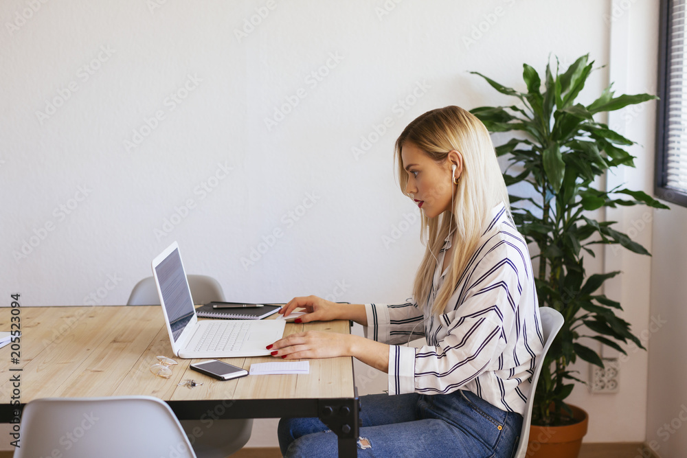 Blond office worker sitting at desk, using laptop Blond office worker sitting at desk, using laptop