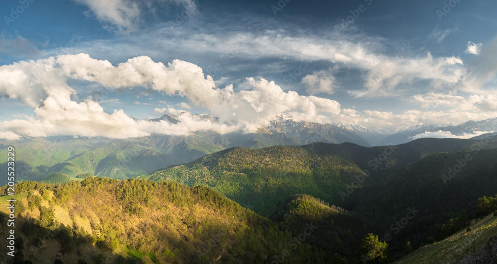 the tops of mountain ranges in the snow and covered by clouds in the summer on a sunny day with meadows and mountain slopes overgrown with trees, the Karachay-Cherkess Republic, the Caucasus
