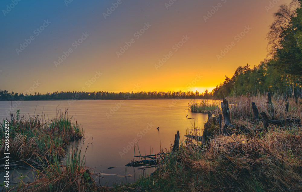 Colorful sunset over the lake in late evening in Spring. Peaceful scenery with clear sky and reflections in water.