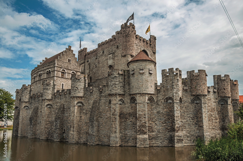 Lake and stone wall in front of Gravensteen Castle on cloudy day in Ghent. In addition to intense cultural life, the city is full of Gothic buildings and Flemish style architecture. Northern Belgium.