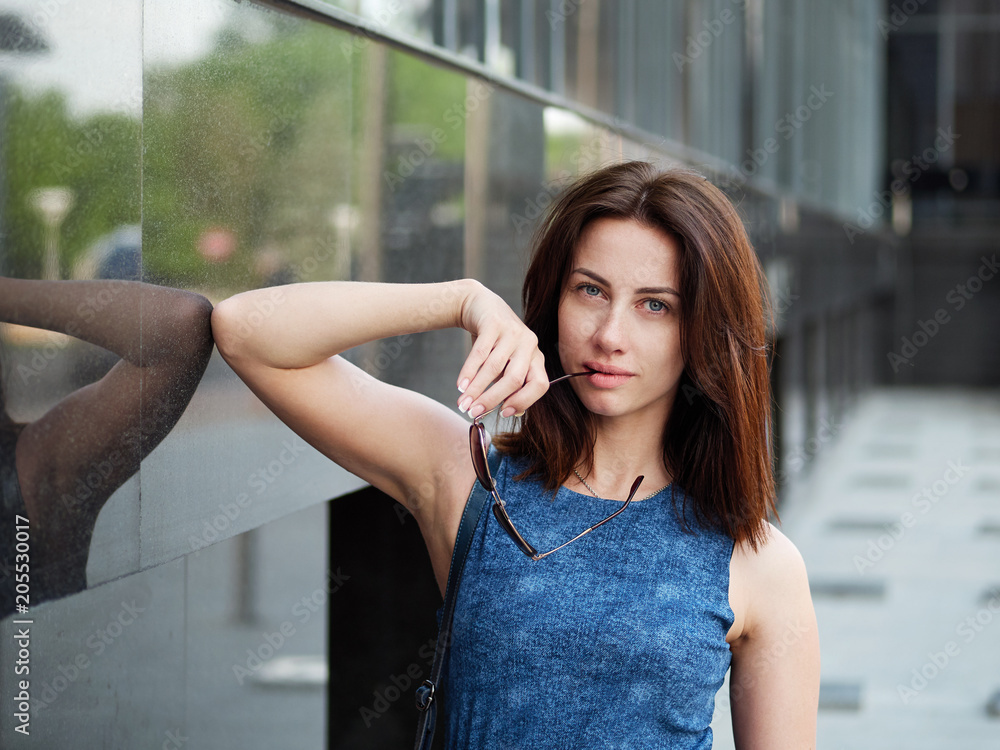 Close up beautiful adult redhead woman in blue jeans dress posing at the street Close up beautiful adult redhead woman in blue jeans dress posing at the street