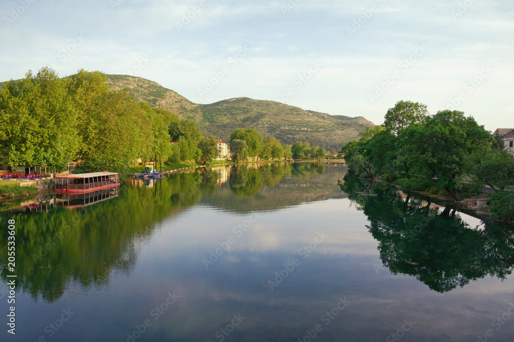 Beautiful landscape with calm river, green trees on banks and their reflection in the water.  Bosnia and Herzegovina, view of Trebisnjica river near Trebinje city