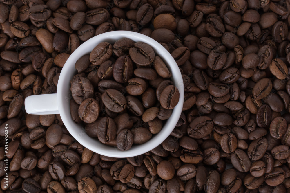 White cup full of coffee beans on the background of coffee beans White cup full of coffee beans on the background of coffee beans