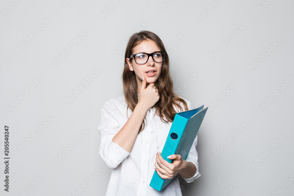 Portrait of office woman wearing white shirt looking upward on copy space and touching chin while holding folder with papers isolated over gray Portrait of office woman wearing white shirt looking upward on copy space and touching chin while holding folder with papers isolated over gray