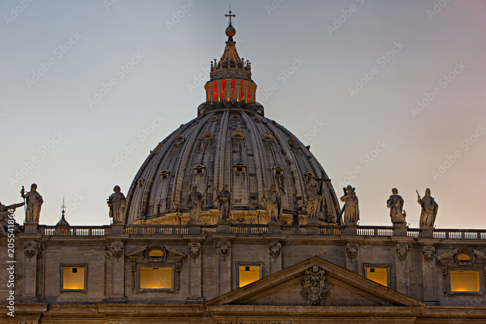 The statues of various Christian Saints and Christ the Redeemer over the main entrance and the dome of St. Peter's Basilica at St. Peter's Square in Vatican City during the blue hour.