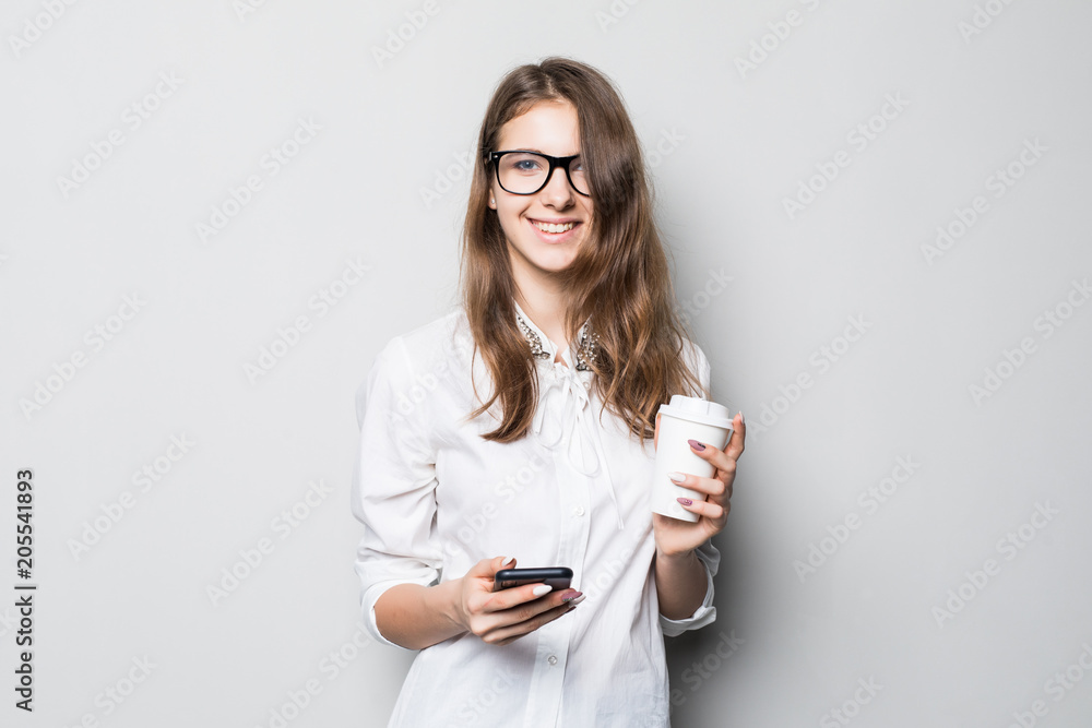 Photo of attractive business woman in formal wear holding mobile phone and takeaway coffee in hands isolated over gray Photo of attractive business woman in formal wear holding mobile phone and takeaway coffee in hands isolated over gray